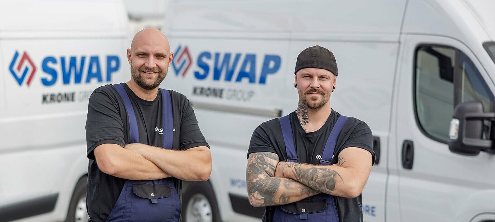 Zwei SWAP Mitarbeiter stehen mit verschränkten Armen vor SWAP Fahrzeugen und blicken in die Kamera